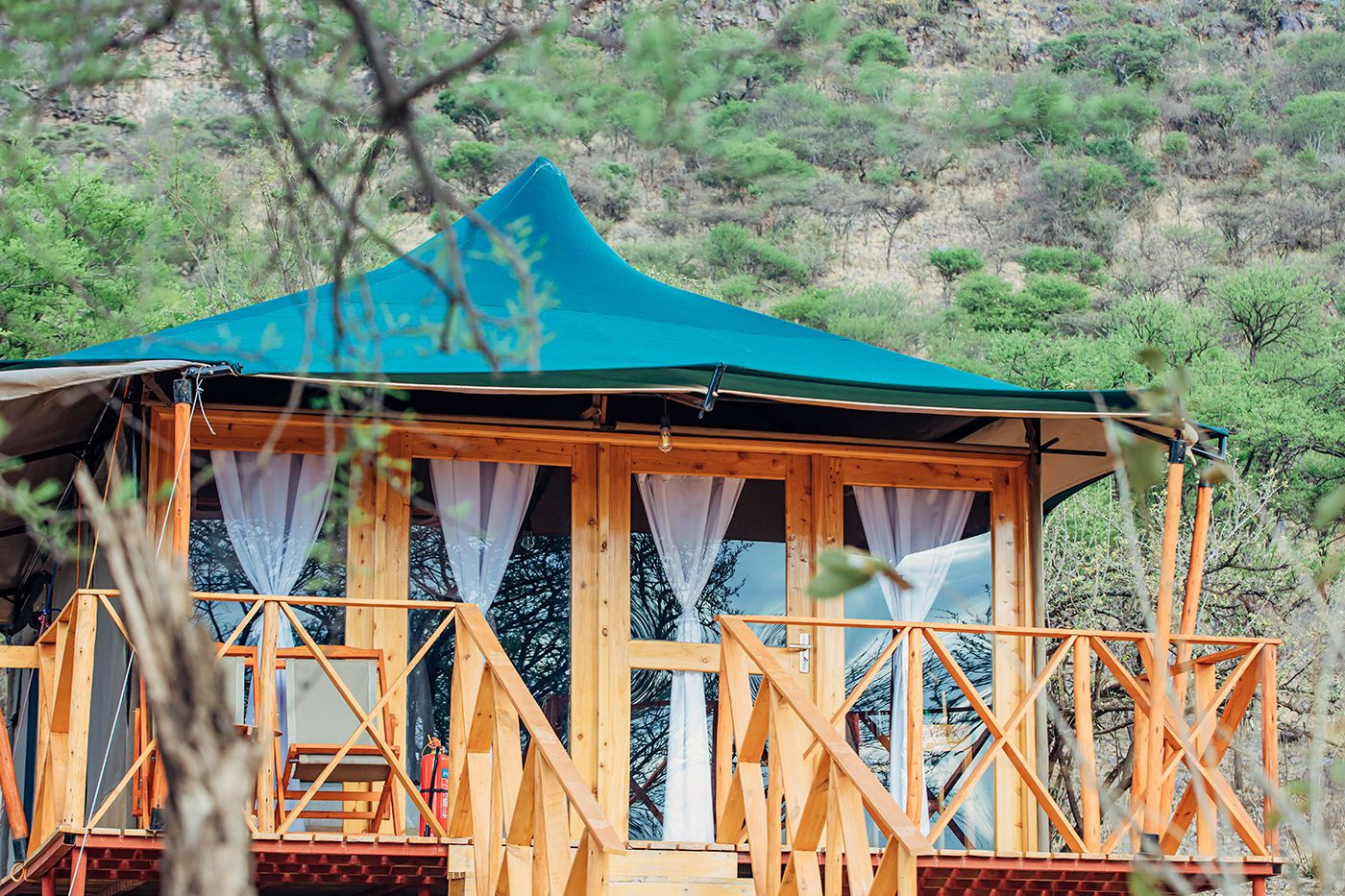 A guest tent with a teal roof and a timber veranda among the trees