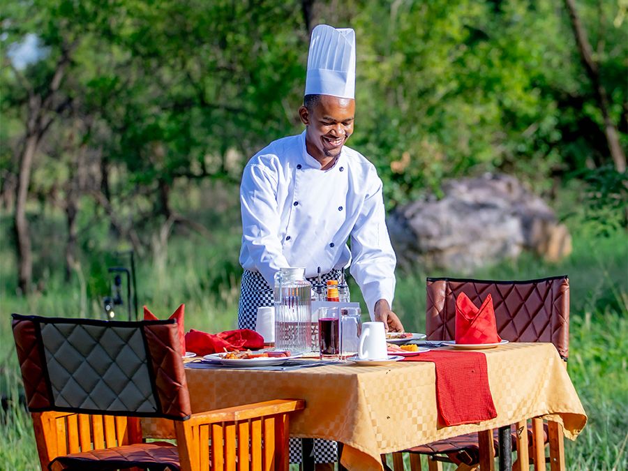 A chef setting a table for a meal in the bush