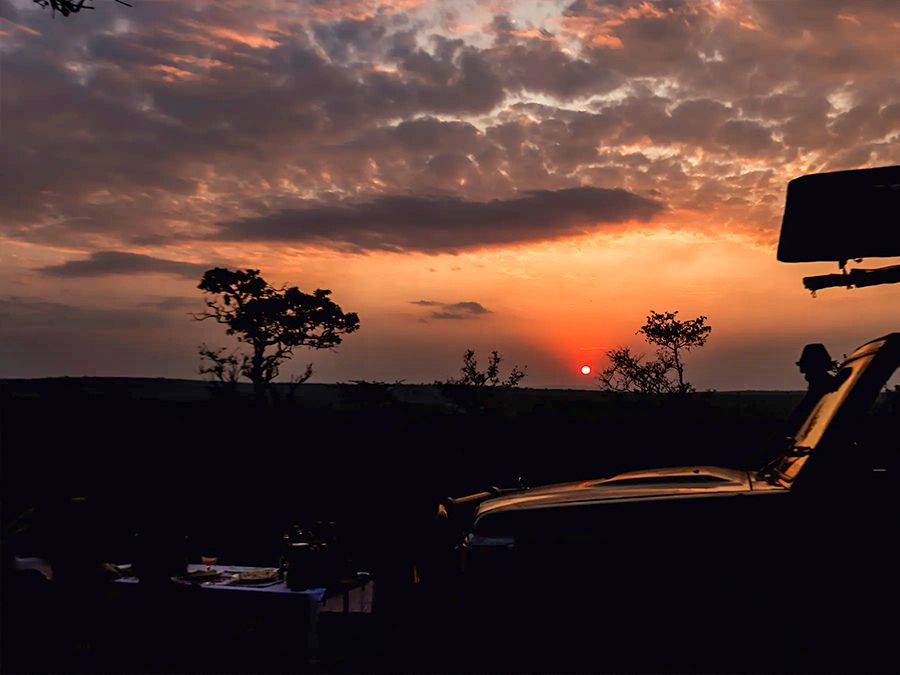 A safari vehicle silhouetted against an orange sky at sundown