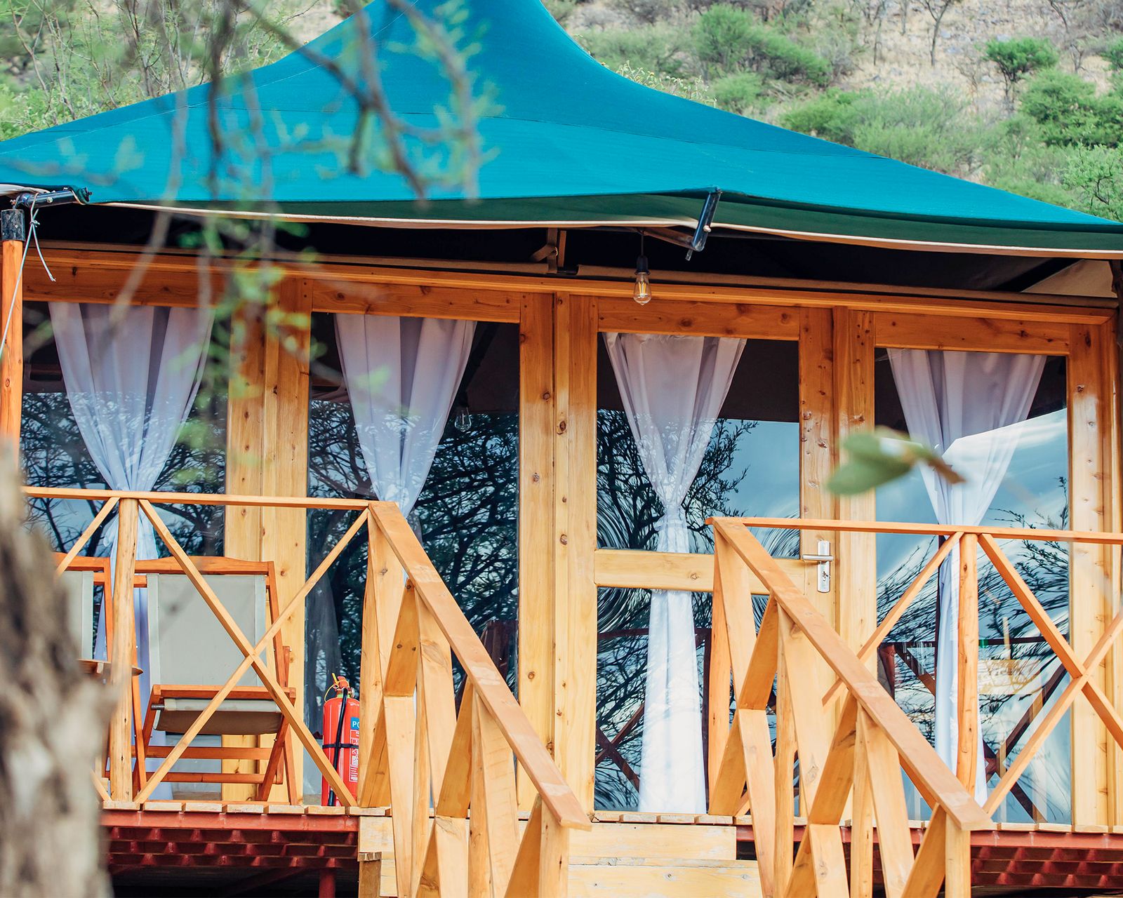 A guest tent with a teal canvas roof and a wooden veranda, framed by acacia branches