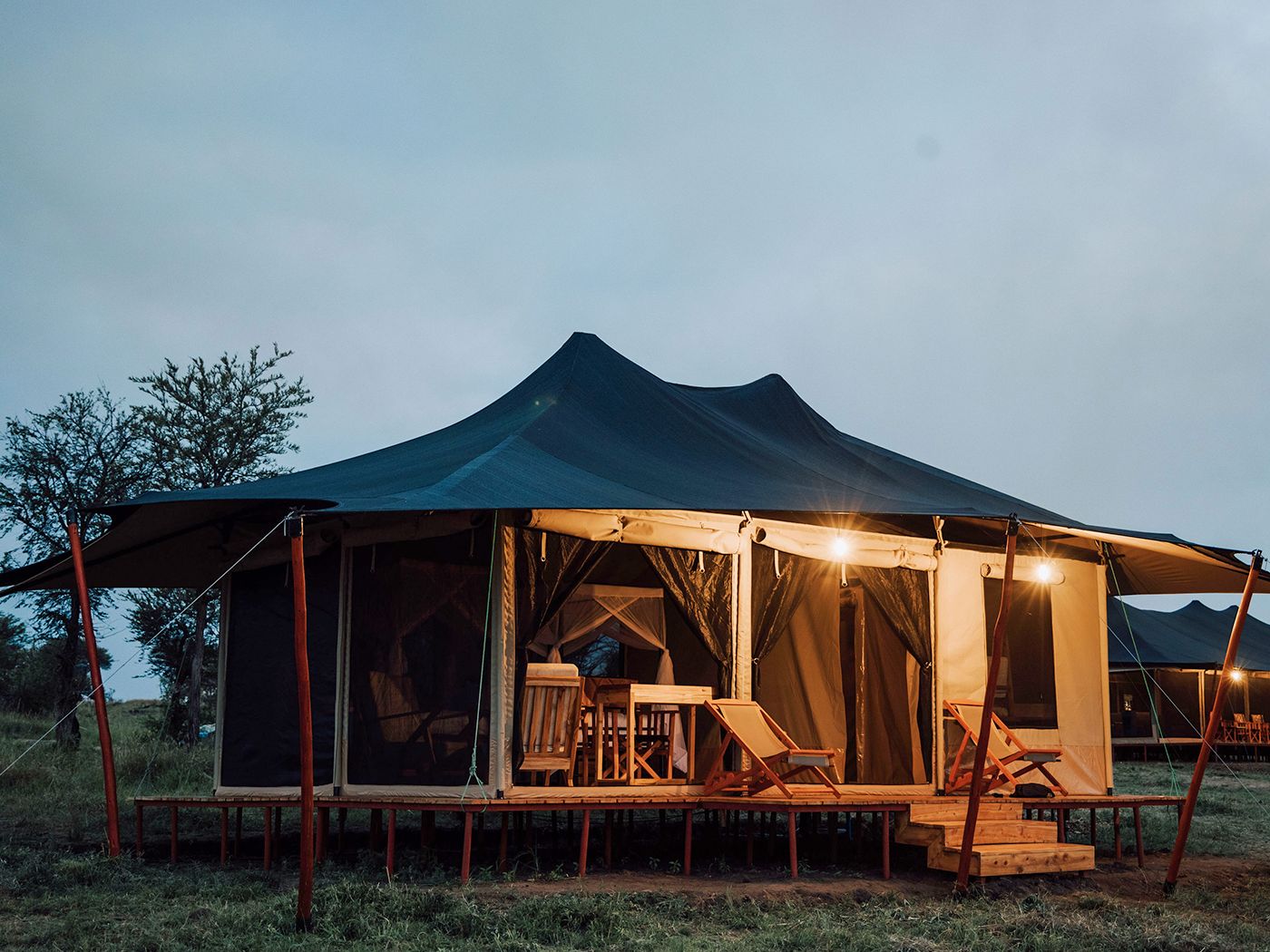 A guest tent at dusk, its veranda lit by warm lights