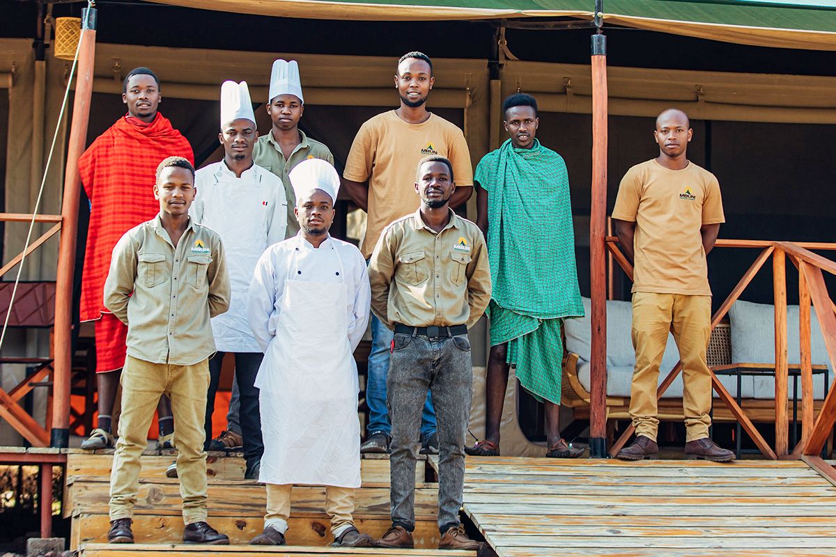 The Mbuni Tented Camps team, including chefs and Maasai staff, standing together on a tent veranda