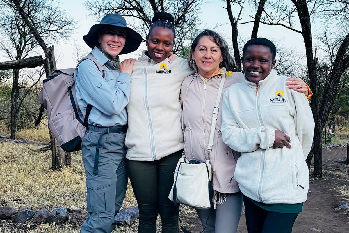 Two guests arm in arm with two members of the team in Mbuni Tented Camps fleeces, on a path through the trees