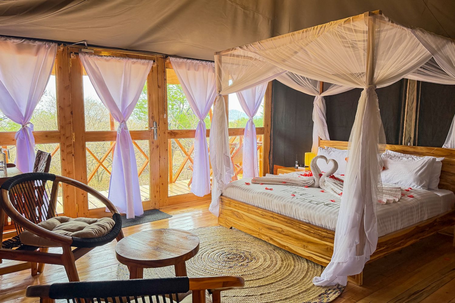 A double bed under a mosquito-net canopy, with two chairs and a small table