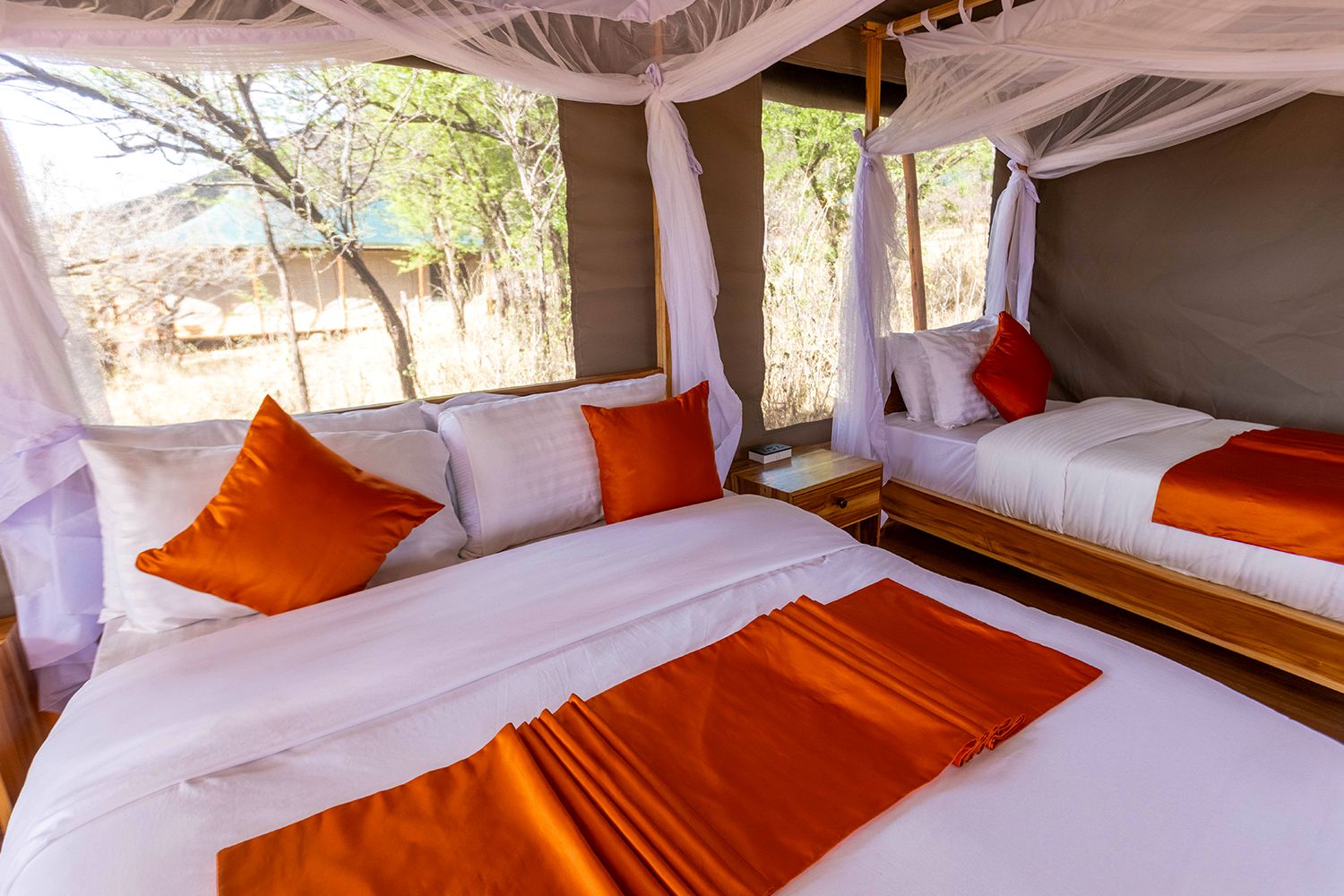 Two beds with orange throws under mosquito-net canopies
